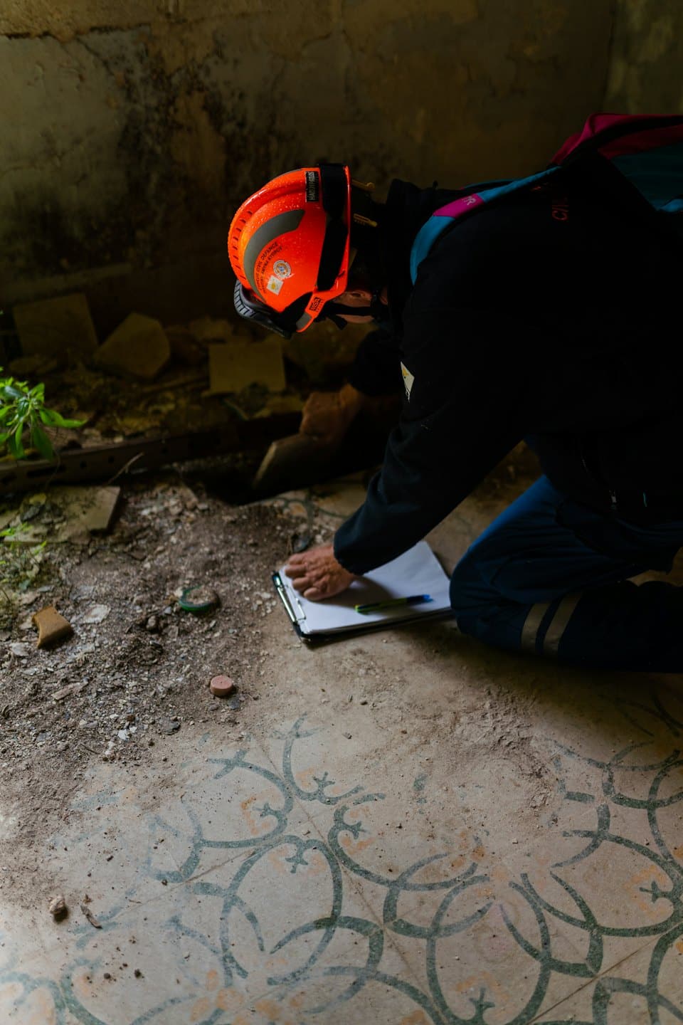 Rescue worker in a hard hat inspects rubble on tiled floors.
