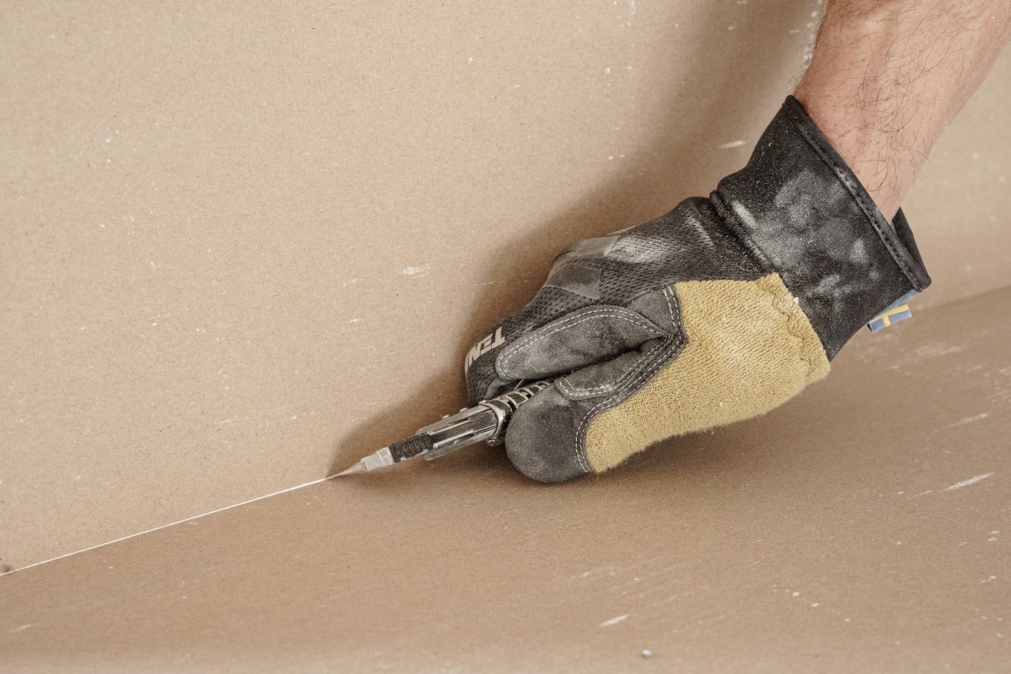 Worker cuts a line into drywall with a utility knife.